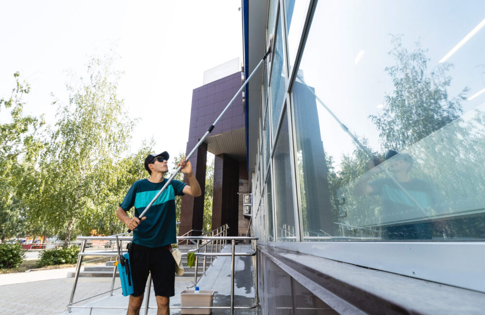 An employee of a professional cleaning service in overalls washes the glass of the windows of the facade of the building. Showcase cleaning for shops and businesses