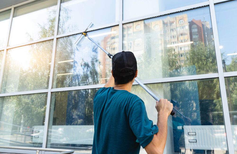 Male professional cleaning service worker in overalls cleans the windows and shop windows of a store with special equipment.