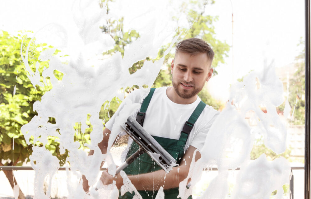 Male cleaner wiping window glass with squeegee from outside